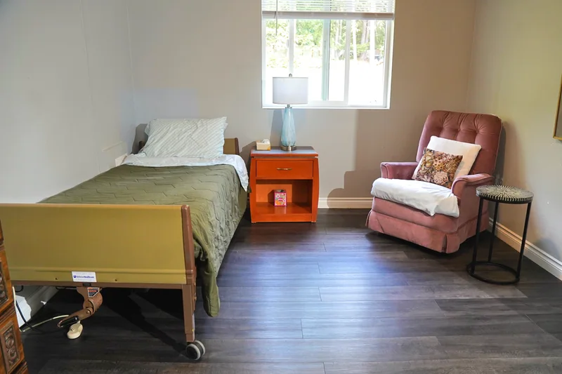 A resident bedroom with an adjustable bed and an armchair by the window